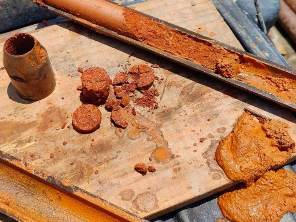 Amostras de solo argiloso retiradas do furo, dispostas sobre prancha ao lado do amostrador