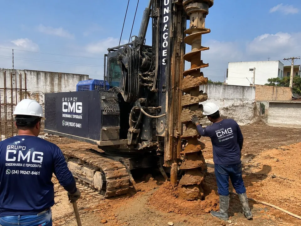 Dois profissionais do Grupo CMG operando a perfuratriz de hélice contínua em obra urbana, com o trado carregado de solo
