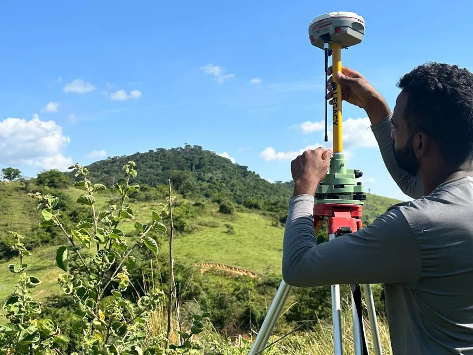 Profissional do Grupo CMG instalando o receptor GNSS no tripé, em terreno de morro