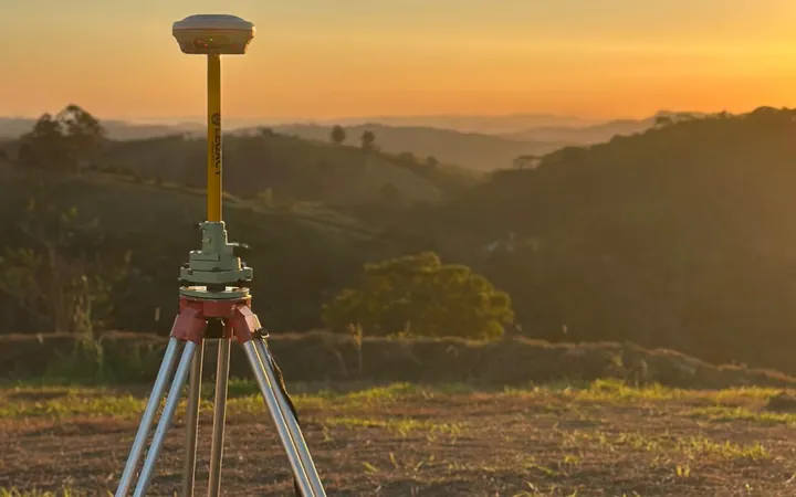 Receptor GNSS/RTK do Grupo CMG estacionado em tripé, em levantamento no fim da tarde com serra ao fundo